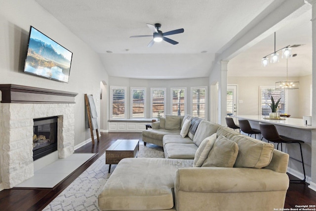 living area featuring a fireplace, baseboards, vaulted ceiling, and dark wood-type flooring