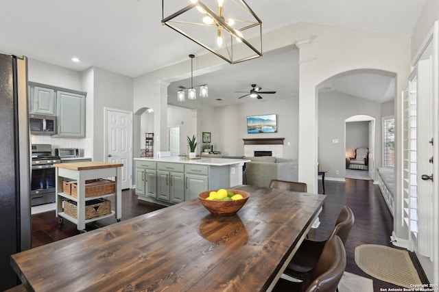 dining space with dark wood-style floors, arched walkways, a fireplace, lofted ceiling, and a ceiling fan