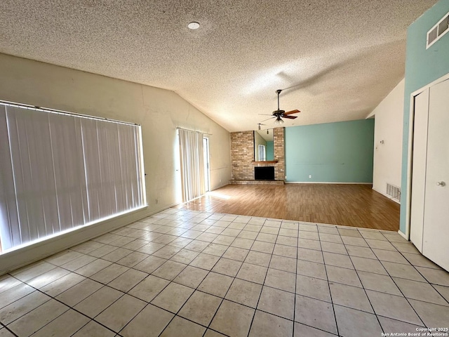 unfurnished living room with visible vents, lofted ceiling, ceiling fan, tile patterned floors, and a fireplace