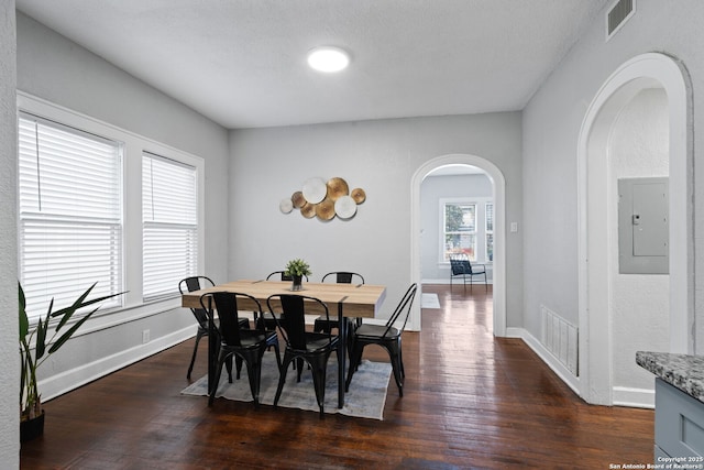 dining space with electric panel, visible vents, arched walkways, and dark wood finished floors