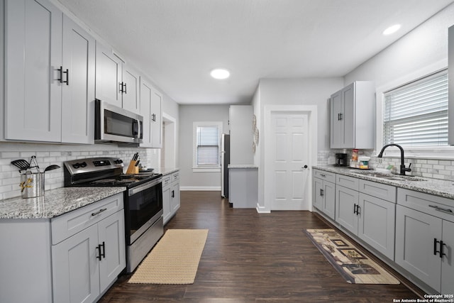 kitchen with dark wood-style floors, appliances with stainless steel finishes, light stone countertops, and a sink