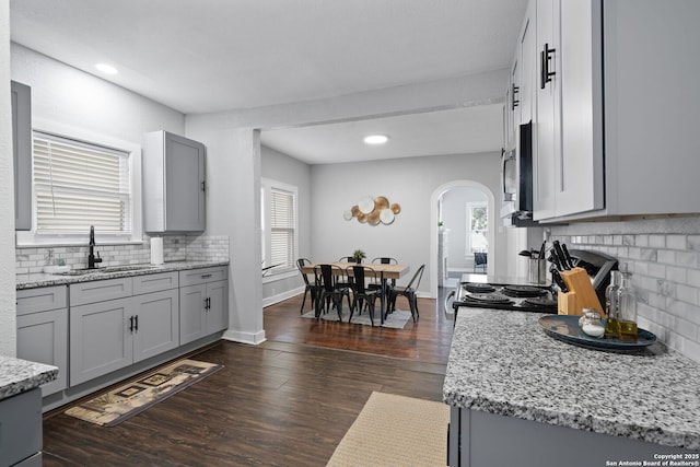 kitchen featuring gray cabinetry, arched walkways, dark wood-style flooring, and a sink