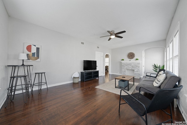 living area featuring wood finished floors, visible vents, a ceiling fan, a fireplace, and arched walkways