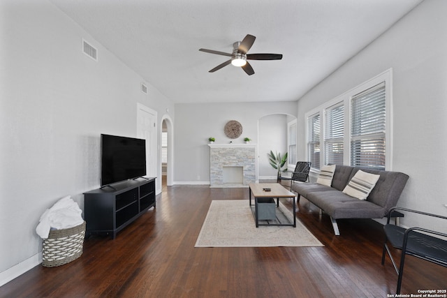 living room with visible vents, arched walkways, a stone fireplace, and wood finished floors