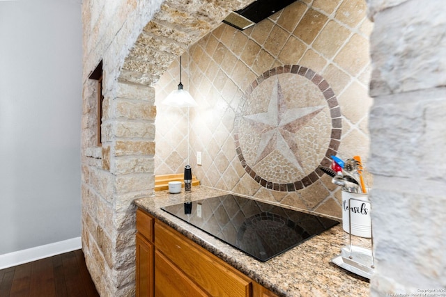 kitchen featuring brown cabinets, backsplash, black electric cooktop, baseboards, and dark wood-style flooring