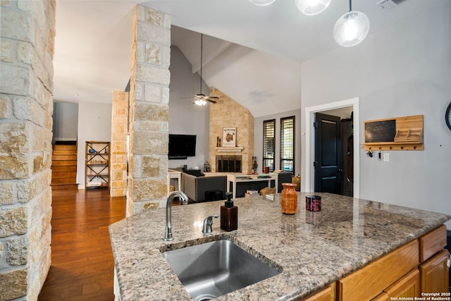 kitchen with a sink, ceiling fan, light stone countertops, a fireplace, and dark wood-style flooring