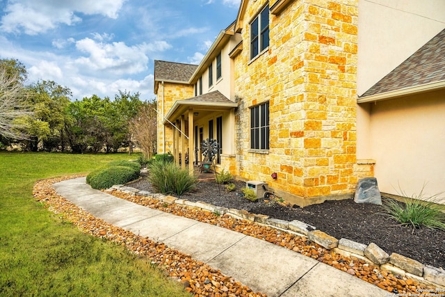 view of side of home with stone siding, stucco siding, a shingled roof, and a yard
