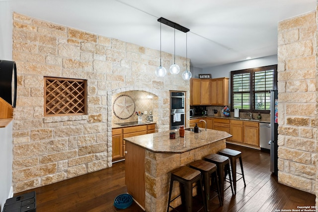 kitchen featuring a sink, stainless steel appliances, dark wood-type flooring, and a center island with sink