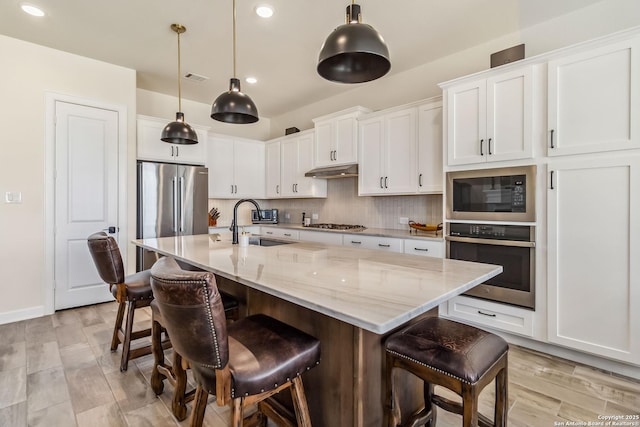 kitchen featuring under cabinet range hood, a sink, white cabinetry, stainless steel appliances, and decorative backsplash