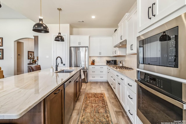 kitchen featuring visible vents, arched walkways, a sink, stainless steel appliances, and under cabinet range hood