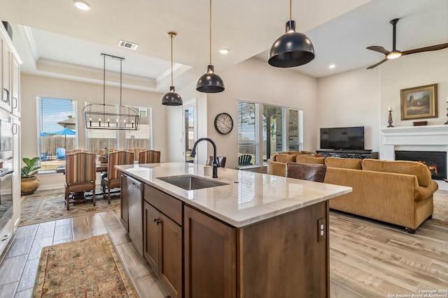 kitchen with visible vents, a sink, a tray ceiling, a warm lit fireplace, and dishwasher