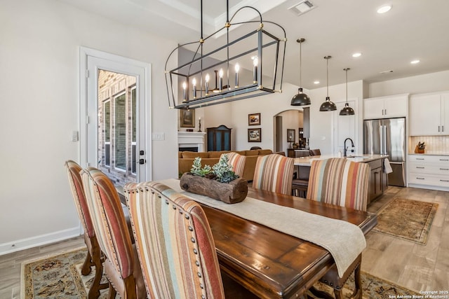 dining area with visible vents, recessed lighting, arched walkways, light wood-style floors, and a fireplace