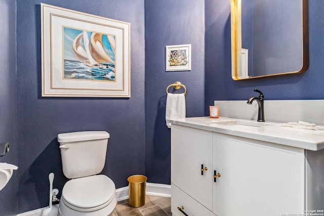 half bathroom with vanity, toilet, baseboards, and tile patterned flooring