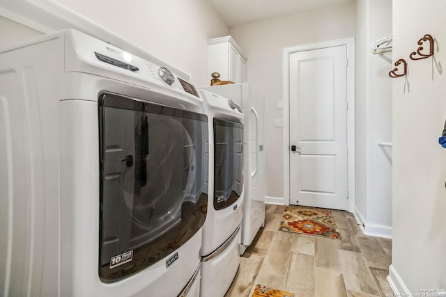 washroom with baseboards, cabinet space, light wood-type flooring, and washer and clothes dryer