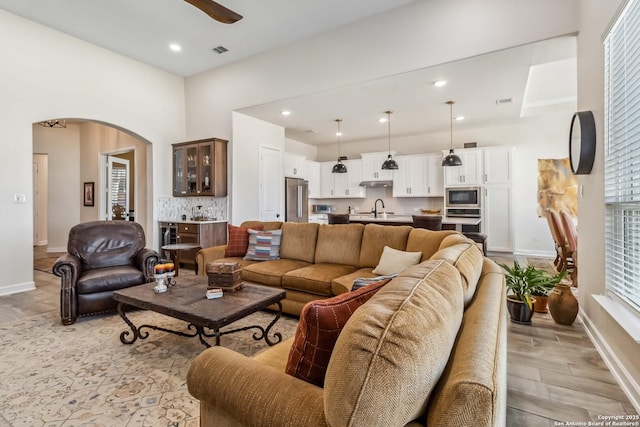 living room with baseboards, recessed lighting, arched walkways, ceiling fan, and light wood-style floors