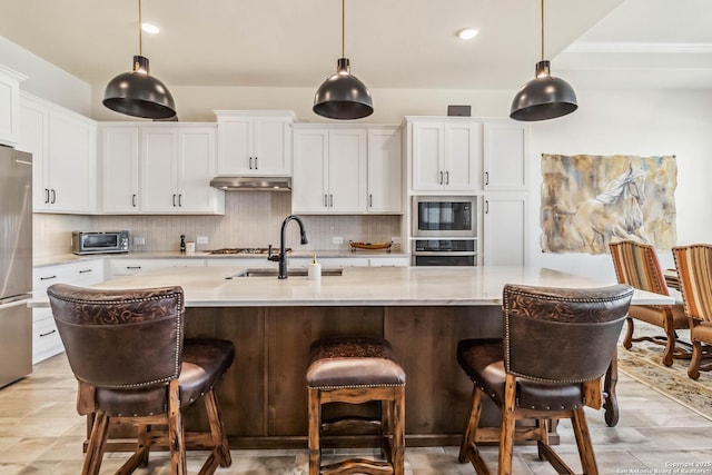 kitchen featuring a sink, decorative backsplash, light countertops, stainless steel appliances, and under cabinet range hood