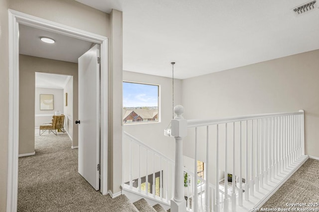 hall featuring an upstairs landing, visible vents, baseboards, and carpet