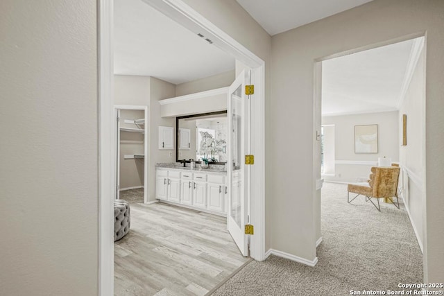 hall with light colored carpet, light wood-style floors, and baseboards