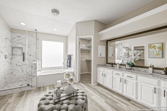 bathroom with a marble finish shower, a walk in closet, double vanity, wood finished floors, and a bath