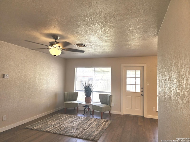 sitting room featuring dark wood-type flooring, a textured wall, visible vents, and baseboards