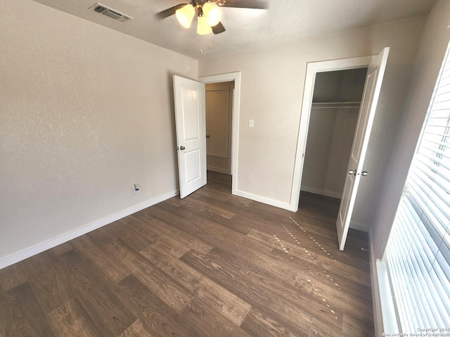 unfurnished bedroom with dark wood-style floors, visible vents, baseboards, ceiling fan, and a closet