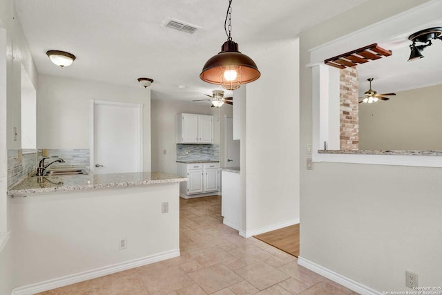 kitchen featuring light stone counters, visible vents, a sink, white cabinetry, and tasteful backsplash