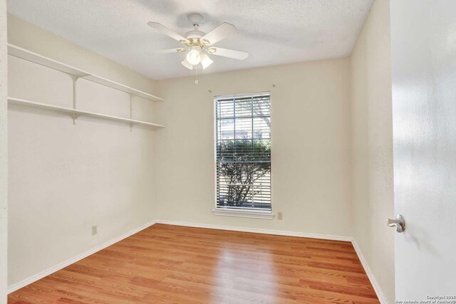 empty room with ceiling fan, baseboards, light wood finished floors, and a textured ceiling