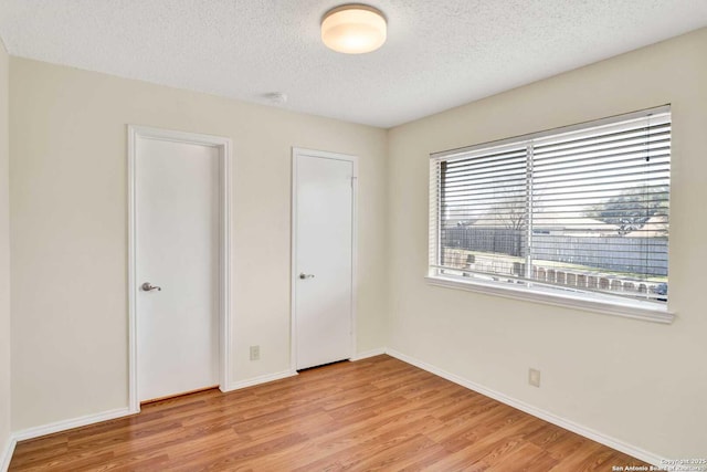 unfurnished bedroom featuring baseboards, light wood finished floors, and a textured ceiling