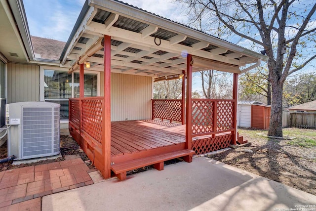 wooden deck with central AC unit, a storage unit, an outdoor structure, and fence