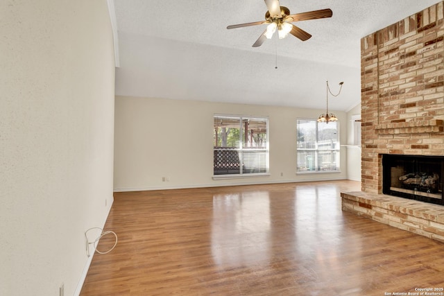 unfurnished living room with lofted ceiling, ceiling fan with notable chandelier, a fireplace, wood finished floors, and a textured ceiling