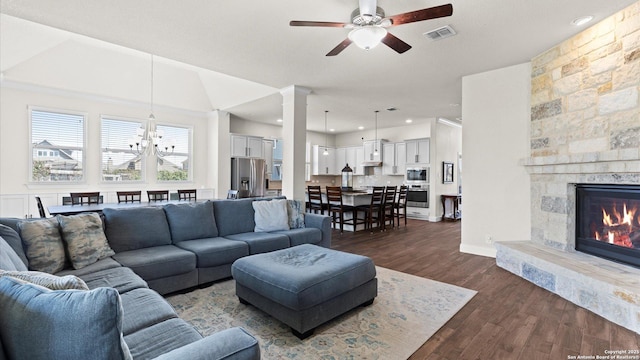 living room featuring visible vents, ceiling fan with notable chandelier, dark wood-style floors, a fireplace, and decorative columns