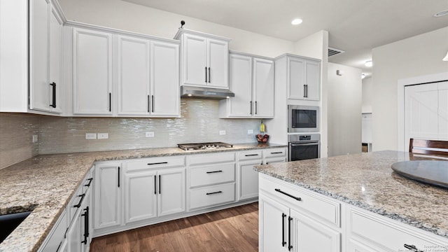 kitchen with backsplash, light stone countertops, under cabinet range hood, wood finished floors, and stainless steel appliances