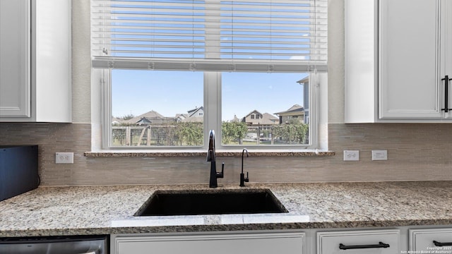 kitchen featuring light stone countertops, a sink, dishwasher, white cabinetry, and backsplash