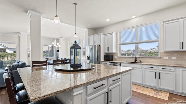 kitchen with a sink, open floor plan, appliances with stainless steel finishes, a breakfast bar area, and dark wood-style flooring