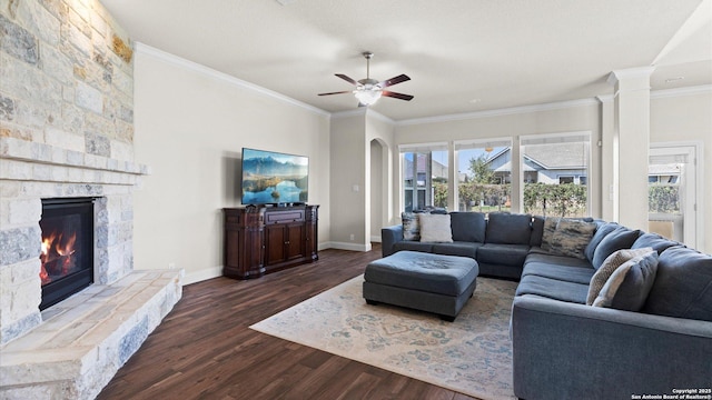 living area with dark wood-style floors, a stone fireplace, crown molding, and baseboards