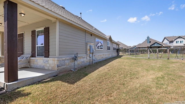 view of side of property with stone siding, a lawn, roof with shingles, and fence