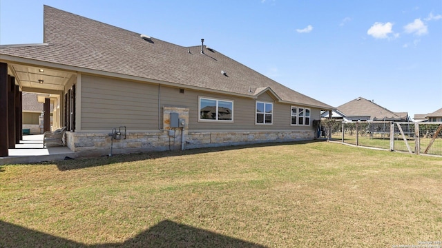 back of property featuring a shingled roof, fence, a lawn, stone siding, and a patio