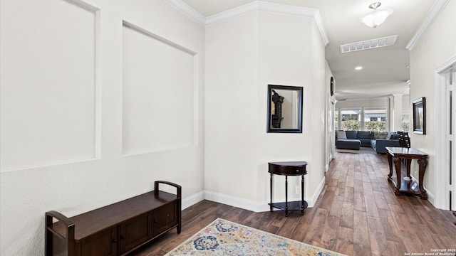 hallway featuring visible vents, wood finished floors, baseboards, and ornamental molding