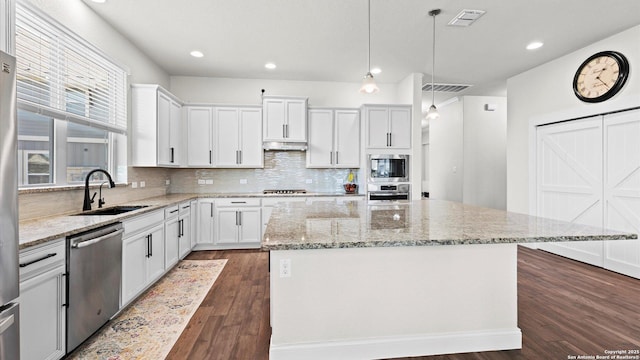 kitchen with a kitchen island, under cabinet range hood, dark wood finished floors, appliances with stainless steel finishes, and a sink