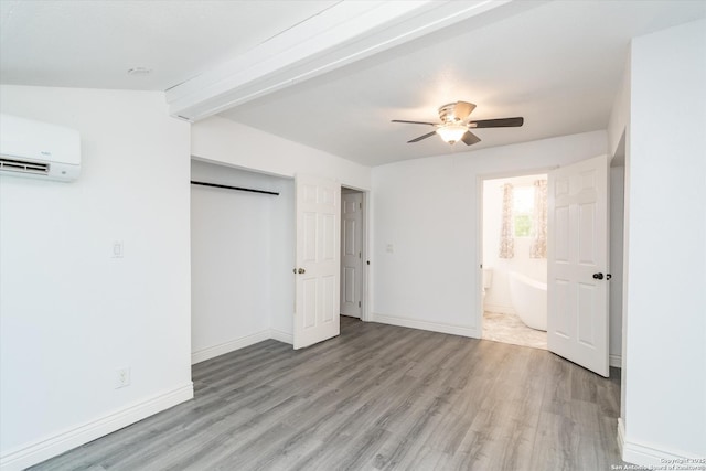 unfurnished bedroom with baseboards, a closet, a wall mounted air conditioner, beamed ceiling, and light wood-type flooring