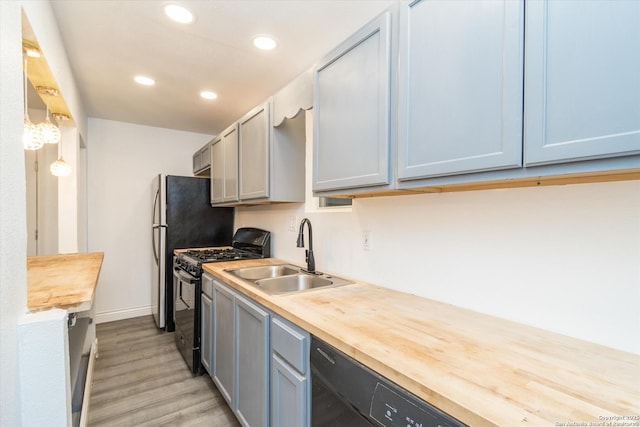 kitchen featuring light wood finished floors, recessed lighting, a sink, butcher block countertops, and black gas range