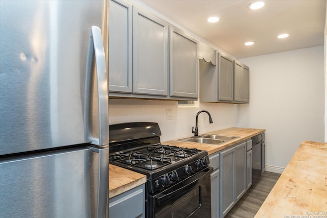 kitchen featuring gray cabinetry, a sink, wood counters, freestanding refrigerator, and black gas range oven