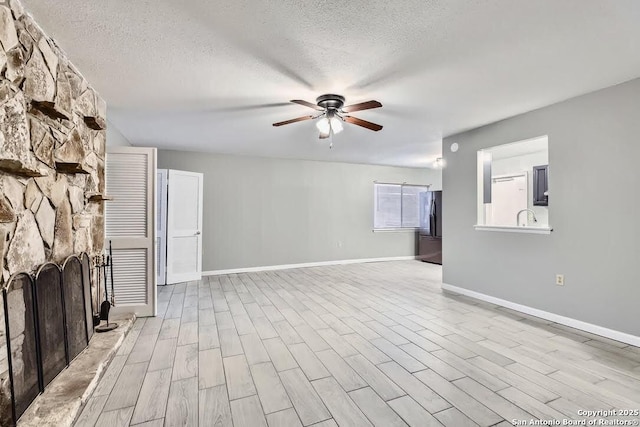 unfurnished living room with a textured ceiling, wood finished floors, a fireplace, and ceiling fan