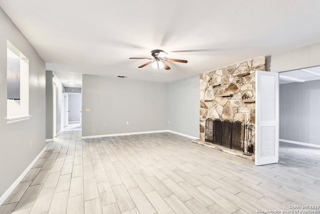 unfurnished living room with visible vents, wood finished floors, a stone fireplace, baseboards, and ceiling fan