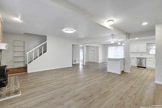 unfurnished living room featuring baseboards, beam ceiling, stairs, and light wood finished floors