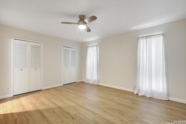 unfurnished bedroom featuring a ceiling fan, wood finished floors, multiple closets, and baseboards