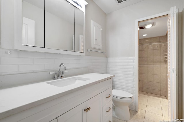 bathroom featuring tile patterned flooring, tile walls, toilet, tiled shower, and vanity