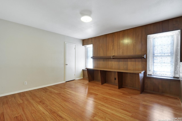 unfurnished office with a wealth of natural light, baseboards, light wood-style flooring, and built in desk