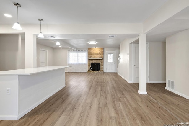 unfurnished living room featuring a brick fireplace, light wood-style floors, visible vents, and baseboards