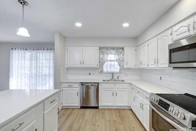 kitchen with a sink, decorative light fixtures, white cabinetry, light wood-style floors, and appliances with stainless steel finishes